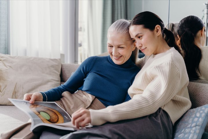 A senior mother and her adult daughter reading together on the couch at home